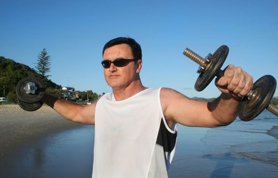 Man works out with weights on the beach just after sunrise.