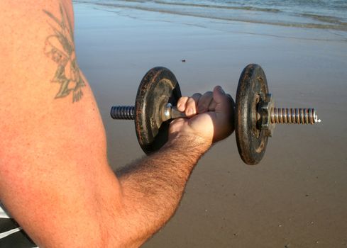 Man works out with weights on the beach just after sunrise.