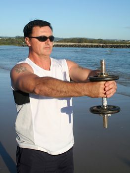 Man works out with weights on the beach just after sunrise.