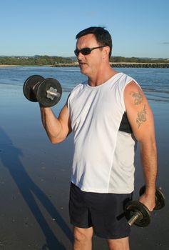 Man works out with weights on the beach just after sunrise.