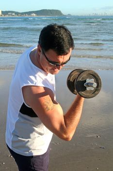 Man works out with weights on the beach just after sunrise.