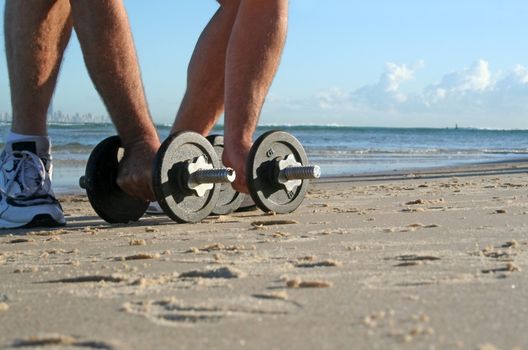 Man picks up work out weights on the beach at sunrise.