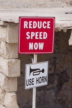 Red sign saying reduce speed now with another sign showing a horn