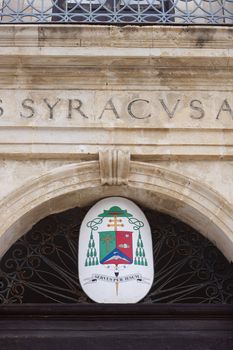 An old coat of arm on a building in Syracuse, saying servus per iesum
