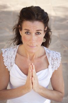 Mature woman with hands together in namaste or prayer, looking at camera