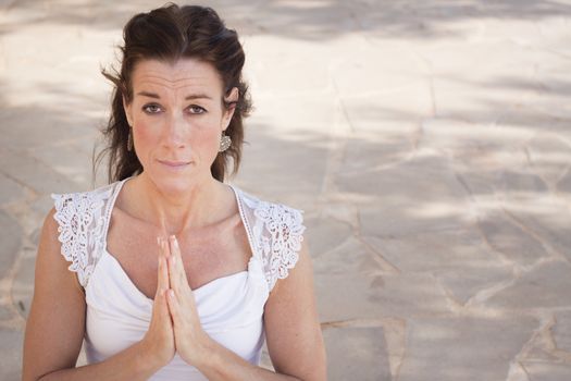 Mature woman with hands together in namaste or prayer, looking at camera. Space for text
