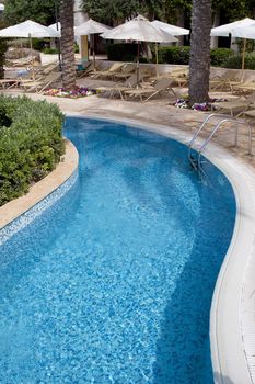 Detail of a curved pool surrounded by trees and sunbeds