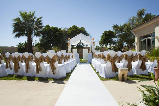 A beautiful garden with palm trees, decorated chairs and a small wedding tent