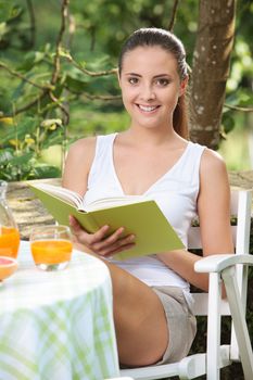 Beautiful smiling girl reading a book outdoors 