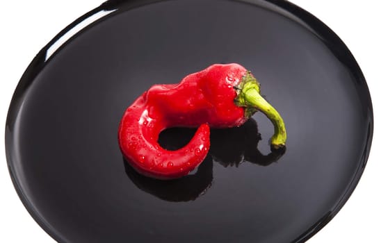 Red fresh chili pepper isolated on black plate