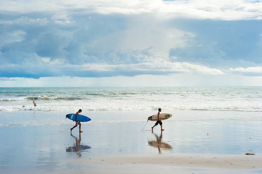 Bali island; Indonesia - March 16, 2013: Local boys walking with a surfboards on the beach. Bali is one of the top of world surfing destinations.