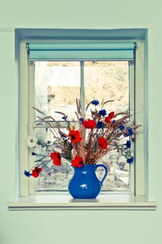 Jug of fresh summer flowers on a window sill