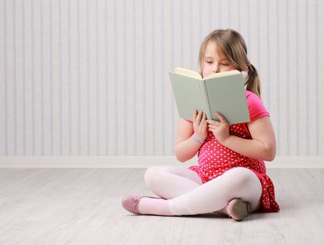 Beautiful little girl reading a book on floor