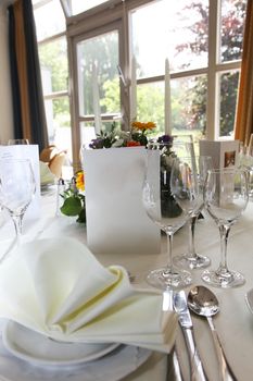 Luxury table setting for a wedding or catered event with silverware and a menu and a view through large windows to a pretty garden