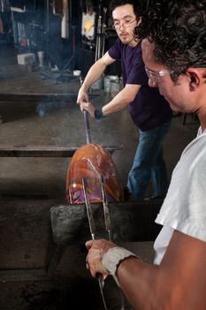Two workers busy with steaming glass vase and tongs