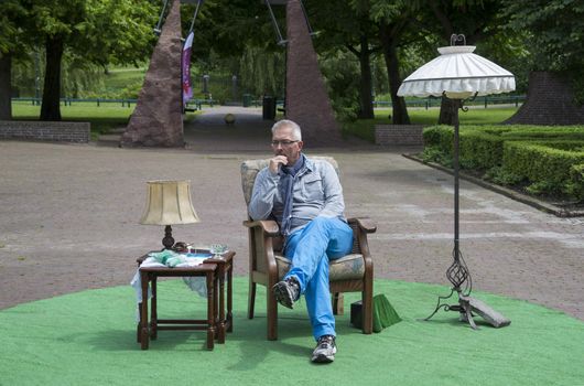 Adult man thinking and sitting on chair in a park with table and lamp