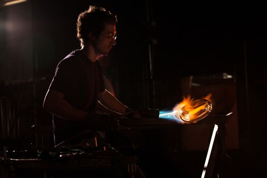 Backlit man with blowtorch shaping glass object