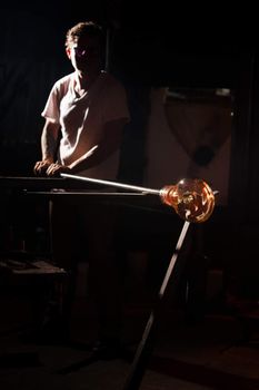 Man working with hot glass object and rod indoors