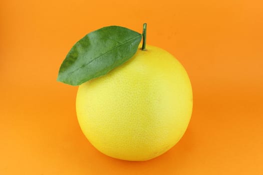 Ripe appetizing grapefruit with leaf on orange background.