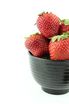 Strawberries into black bowl isolated over white background
