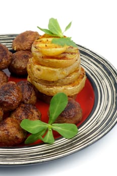 Roasted Meatballs and Stack of Grilled Potato with Greens on Red Striped Plate closeup on white background