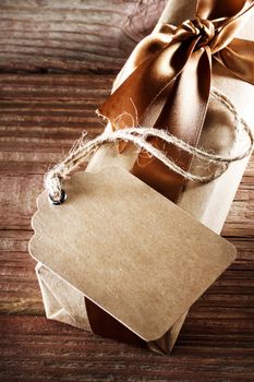 Handmade paper tag with present box with a brown ribbon on a rustic wooden table