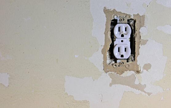 A dirty electrical outlet exposed during a renovation and the surrounding dry wall. 
