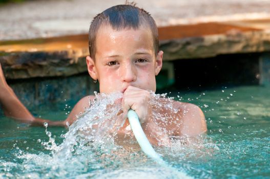 Cute young boy in swimming pool with water hose in his mouth.