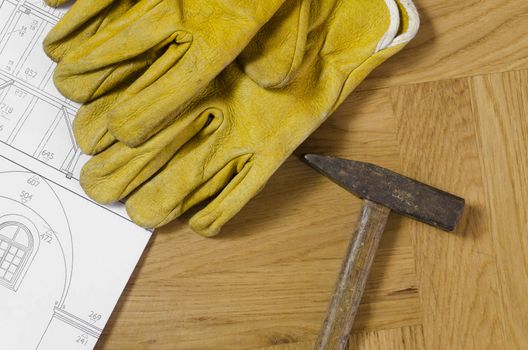 building plans with hammer and working gloves on wooden floor