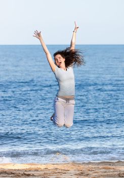 A beautiful happy woman jumping of joy on a beach.