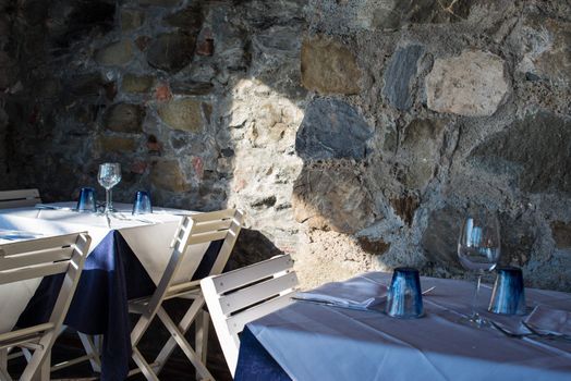 Tables set for cozy dinner with blue glasses, wine glasses and cutlery