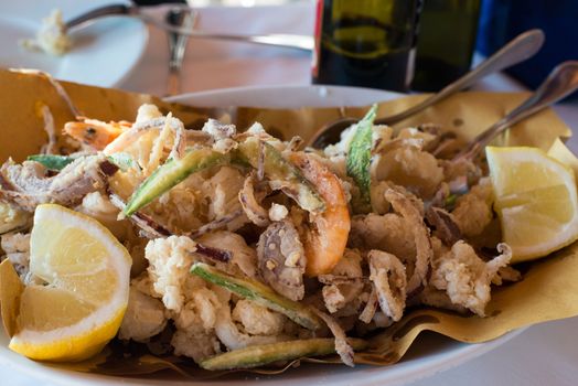 Deep batter fried seafood, squid rings , calamari and scampi with vegetables and lemons on white plate in a restaurant
