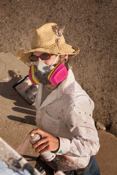 Person with hat and sunglasses spray painting a wall