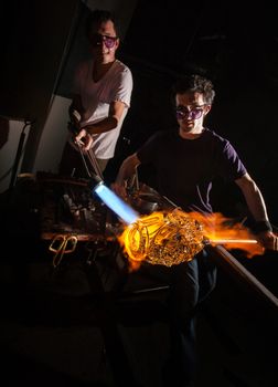 Men working with flaming blowtorch on glass art piece