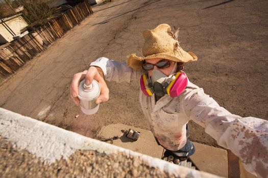 Graffiti artist in hat and sunglasses spray painting