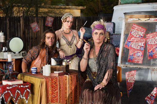 Trio of serious fortune tellers sitting outside with table