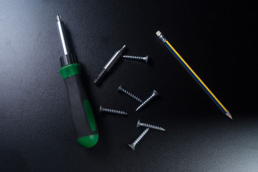 Screws, screwdriver and pencil on black background.