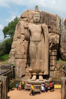KEKIRAWA, SRI LANKA - APR 16: Pilgrims pray near Avukana standing Buddha statue on Apr 16, 2013 in Sri Lanka. It is 40 feet (12 m) high, has been carved out of a large granite rock in the 5th century.