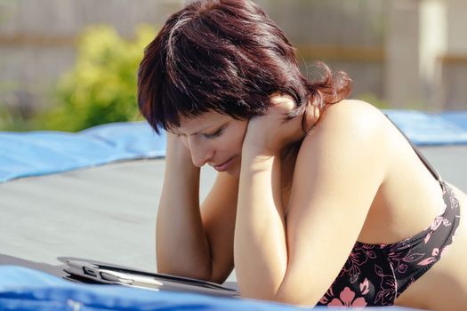 busty woman with swimsuit reading news on tablet outdoor