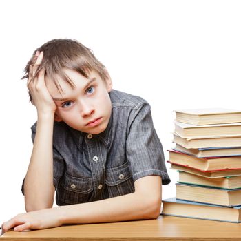 Portrait of upset schoolboy sitting at desk with books holding his head