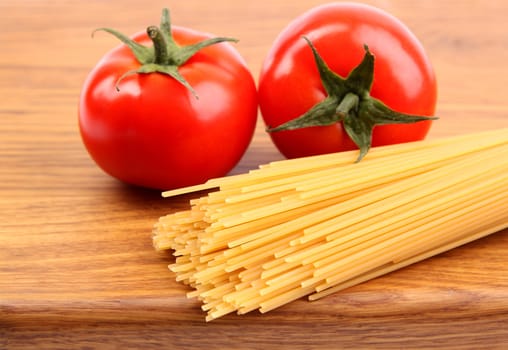 Tomatoesl and uncooked spaghetti on a cutting board close-up