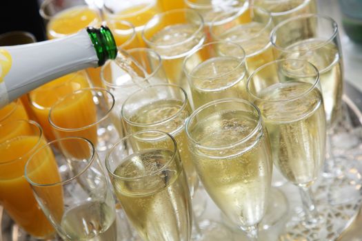 Closeup of the neck of a bottle pouring champagne into elegant glass flutes on a wedding buffet with glasses of fresh orange juice alongside