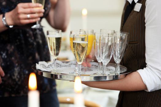 Closeup of the hands of a waiter carrying a tray serving champagne and orange juice to guests at a catered function or wedding