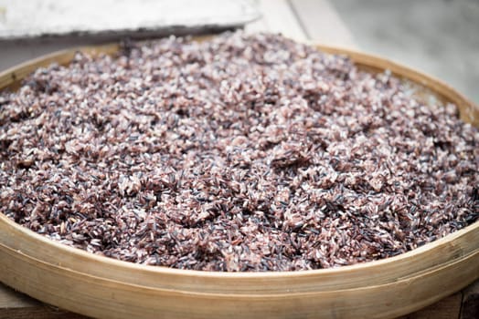 Cooked steam black rice in big wooden plate dish with shallow depth of field