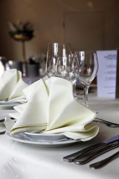 Closeup of and elegant table setting with cutlery and glasses for a variety of courses and decoratively folded cream linen napkin