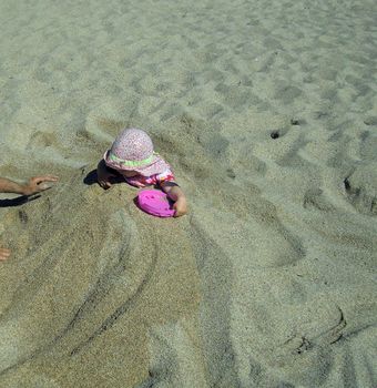 Portrait of little cute blond girl (one year and seven months of age) buried in the sand