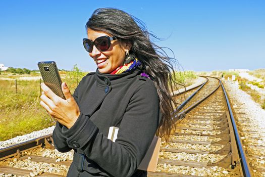 Young beautiful woman is reading a text message on a railroad track