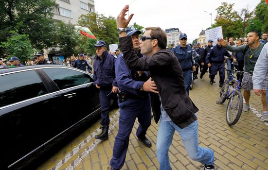 Sofia; Bulgaria - June 26, 2013: Policeman is garding the vehicle of the minister of interior from a protester near bulgarian parliament. On the 12th day of the protest originally sparked by the controversial appointment of businessman and MP Delyan Peevski as the new head of the State Agency for National Security, protestors had ocupated the Parliament and the police had to secure deputates and ministers exiting.