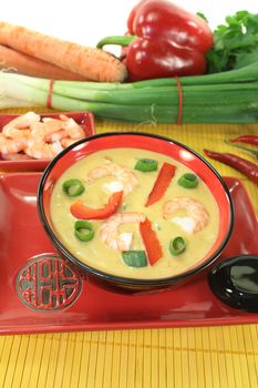 Curry soup with shrimp, red pepper, leeks and coconut milk on bright background