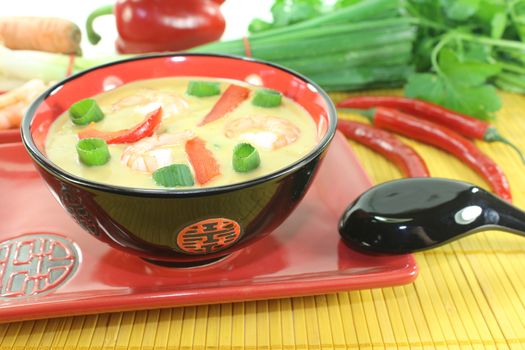 Curry soup with shrimp, red pepper, chili, leeks and coconut milk on light background